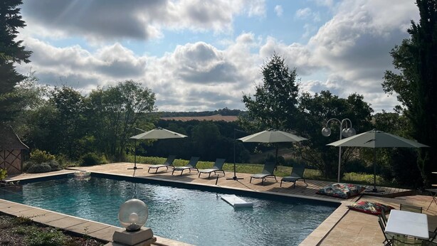 Ein rechteckiger Pool mit Liegestühlen und Sonnenschirmen, umgeben von einer Holzterrasse und einer Steinmauer.