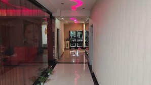 Un pasillo con piso reflectante, una pared divisoria de vidrio a la izquierda y una luz de neón rosa en el techo.