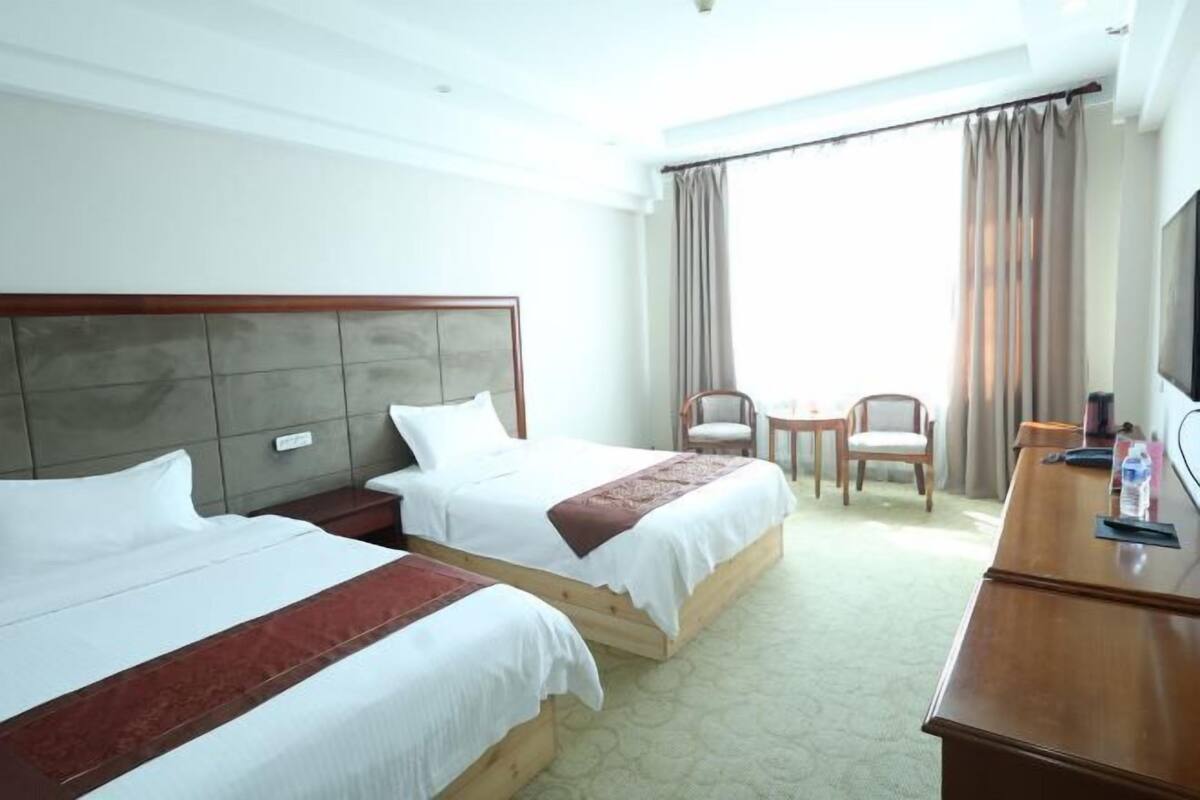 Une chambre d’hôtel avec deux lits, un bureau, une chaise, une télévision et une fenêtre avec des rideaux.
