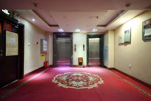 Ein Hotelgang mit rotem Teppich, zwei Aufzügen und Sicherheitseinrichtungen.