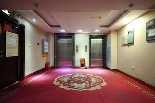 Pasillo de hotel con alfombra roja, dos ascensores y equipo de emergencia.