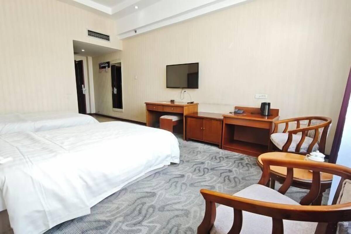Une chambre d’hôtel avec un lit, un bureau, une chaise, une télévision et un sol recouvert de moquette.
