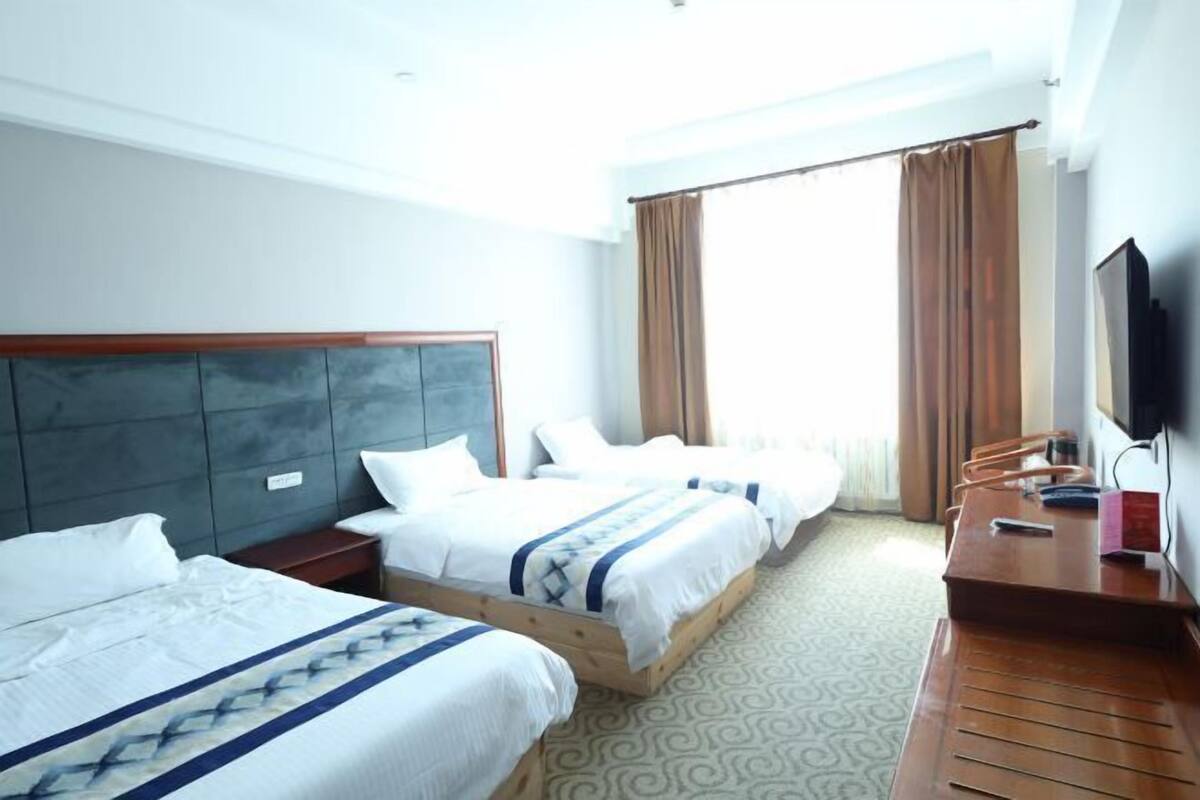 Une chambre d’hôtel avec deux lits, un bureau, une chaise, une télévision et une fenêtre avec des rideaux.