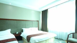 Habitación de hotel con dos camas, cabecera de madera, mesita de noche, una silla y un amplio ventanal con cortinas.