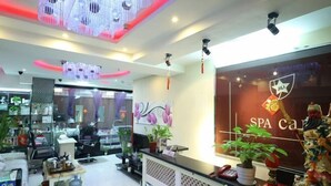 Un área de recepción de spa con diseño moderno, que incluye un mostrador de recepción, plantas en macetas y una estatua decorativa.