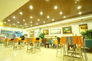 A restaurant with a high ceiling, multiple tables with orange tablecloths, and a clean, tiled floor. - Suifenhe Jixing Hotel (Suifenhe)