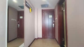 A hallway with a wooden door, a coat rack, and a vent on the ceiling.