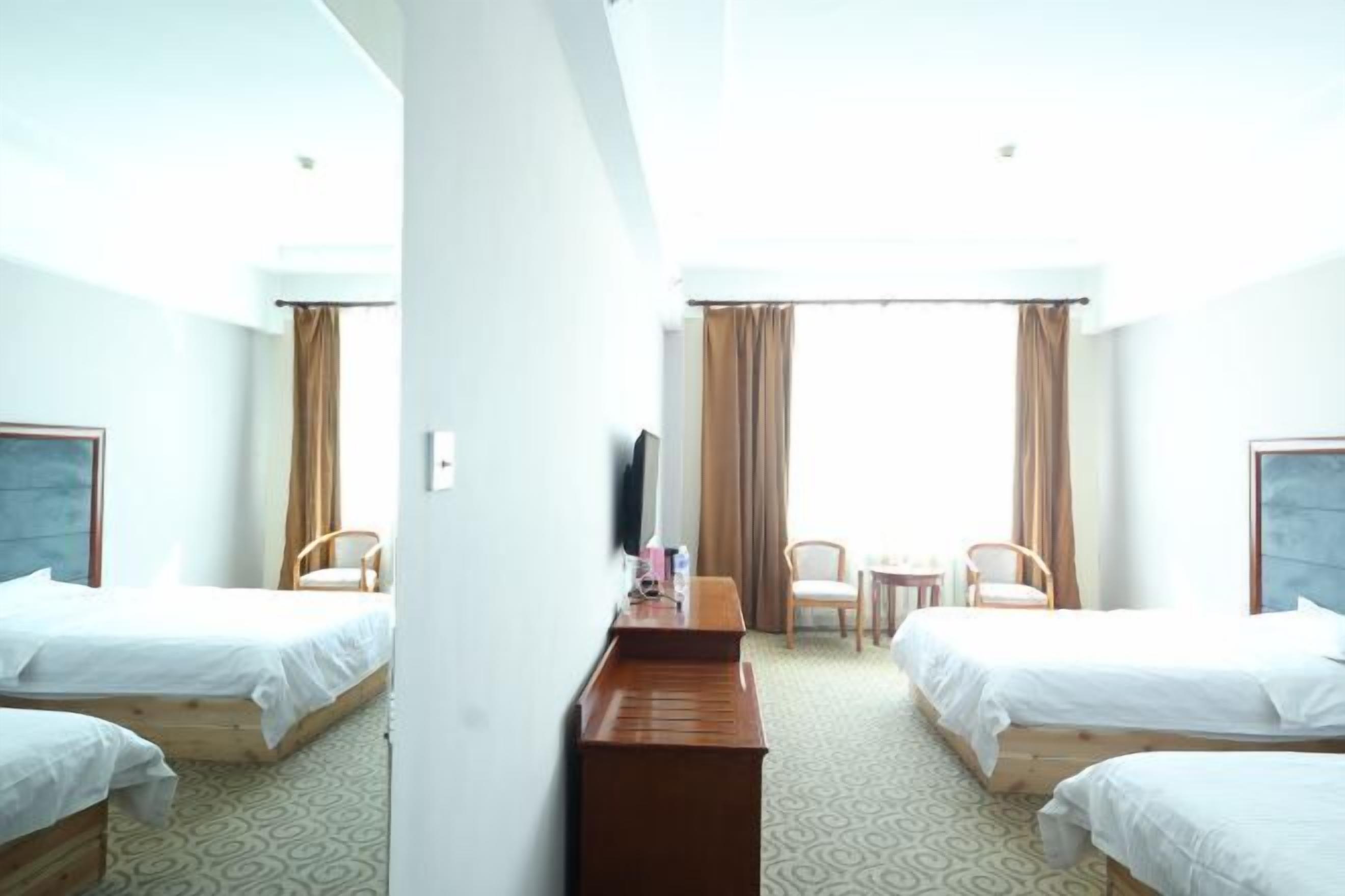 Ein Hotelzimmer mit zwei Einzelbetten, einem Schreibtisch, einem Stuhl, einem Fernseher und einem Fenster mit Vorhängen.
