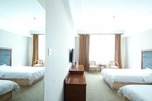 A hotel room with two single beds, a desk, a chair, a TV, and a window with curtains.