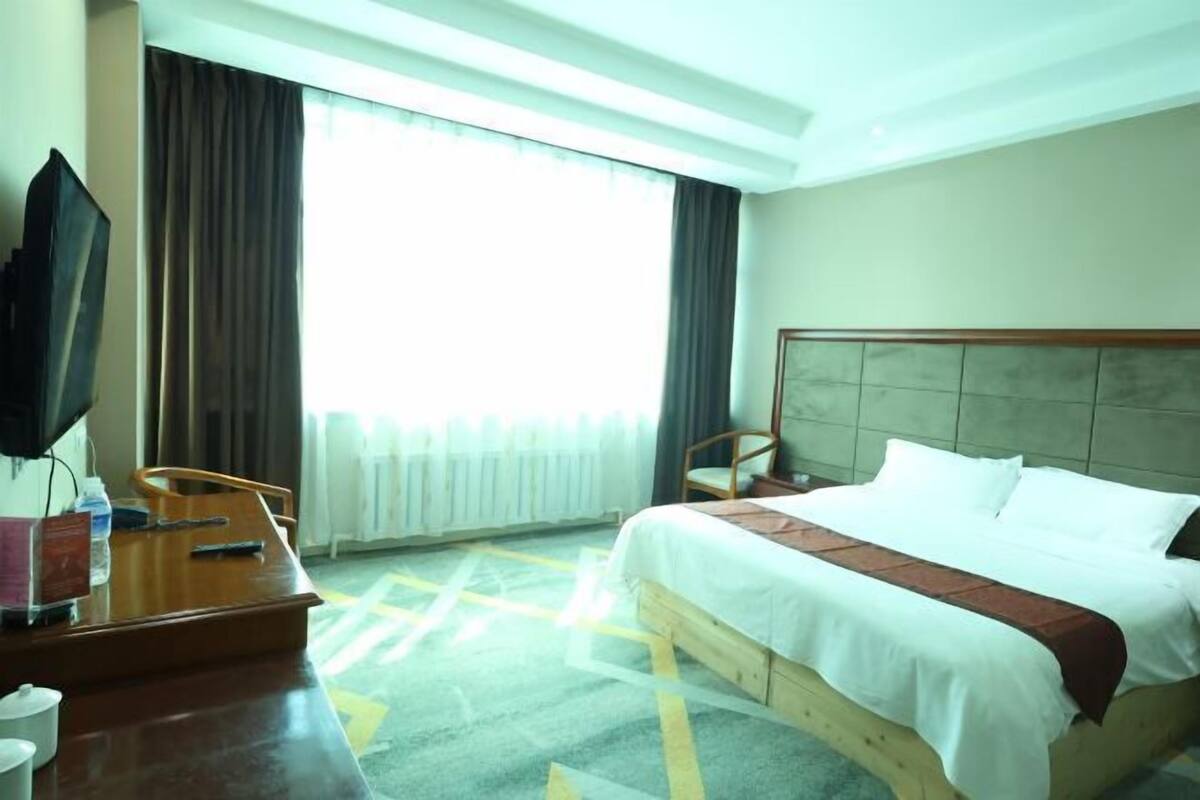 Une chambre d’hôtel avec un lit, un bureau avec une télévision, une chaise et une grande fenêtre avec des rideaux.