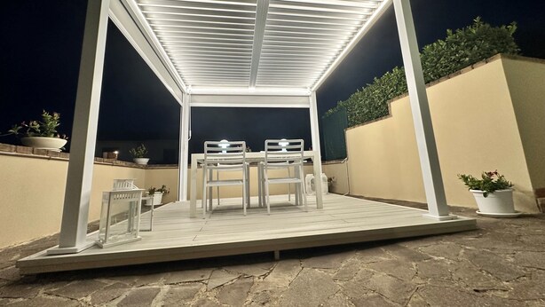 A covered outdoor patio with a table and chairs, potted plants, and a stone floor.