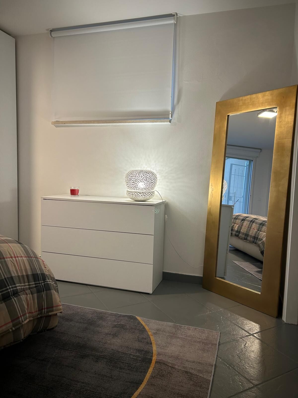 A bedroom with a white dresser, a mirror with a gold frame, and a bed with a plaid blanket.