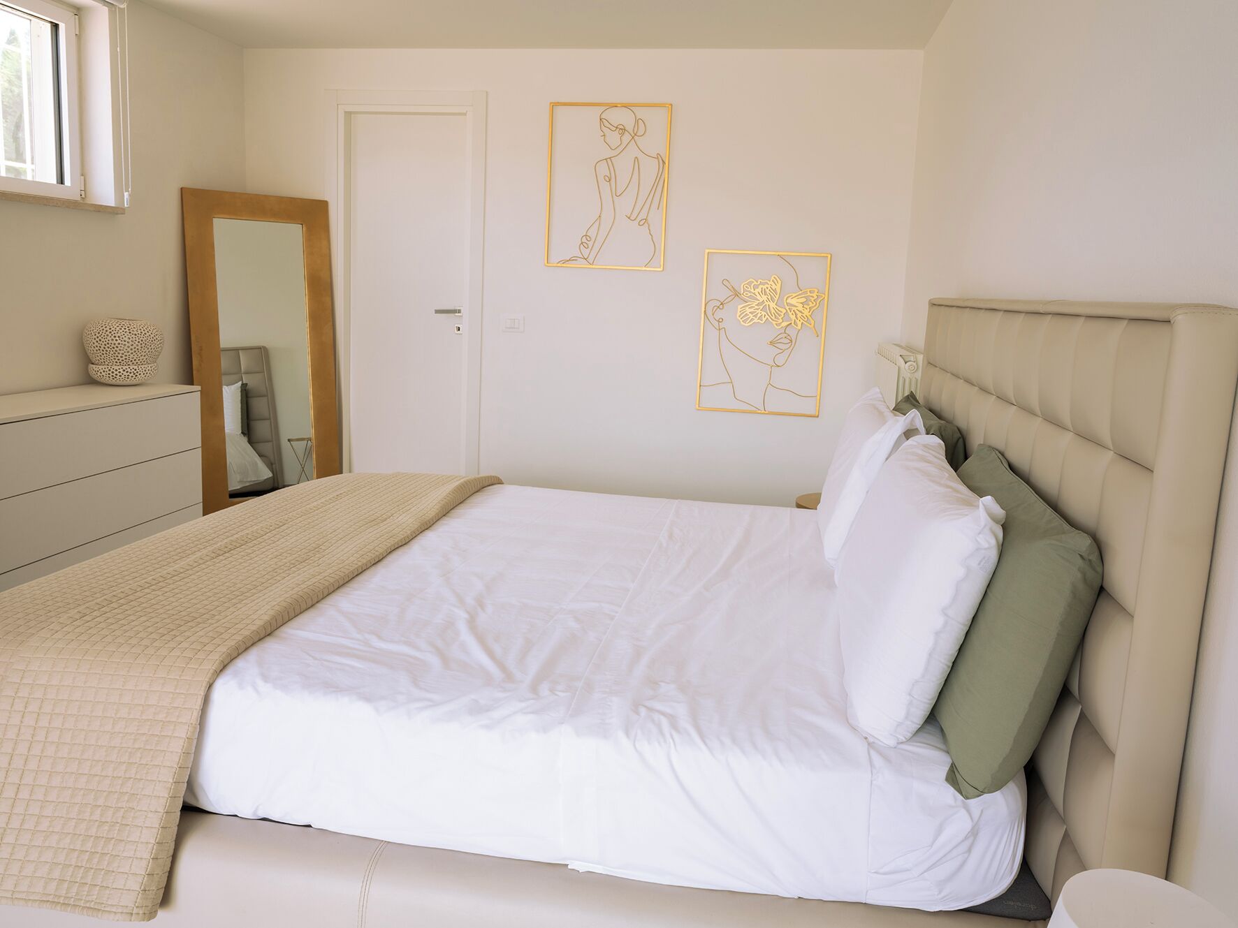 Un dormitorio con cama, cómoda, espejo y dos cuadros en la pared.
