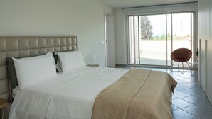A bedroom with a large bed, a nightstand, a chair, and a sliding glass door leading to a balcony.