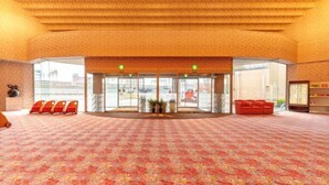 A hotel lobby with a patterned carpet, a central seating area with red chairs, and a glass entrance.