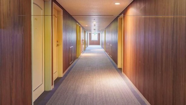 A long, narrow hallway with wooden paneling on the walls and carpeted floor.
