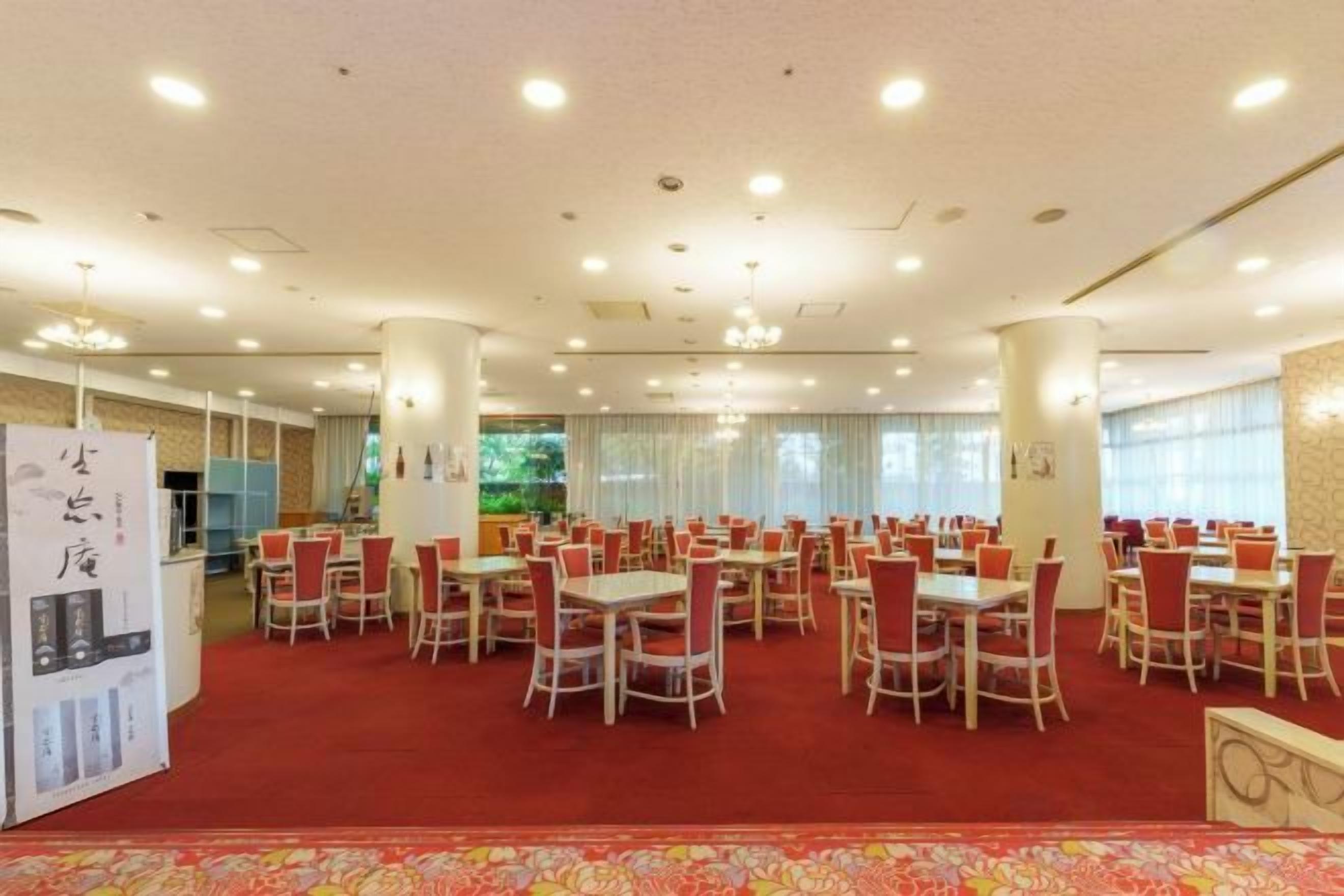 A spacious dining area with multiple tables and chairs, a red carpet, and a white ceiling with recessed lighting.