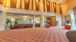 A spacious hotel lobby with a patterned carpet, a seating area with tables and chairs, and a large window providing natural light.