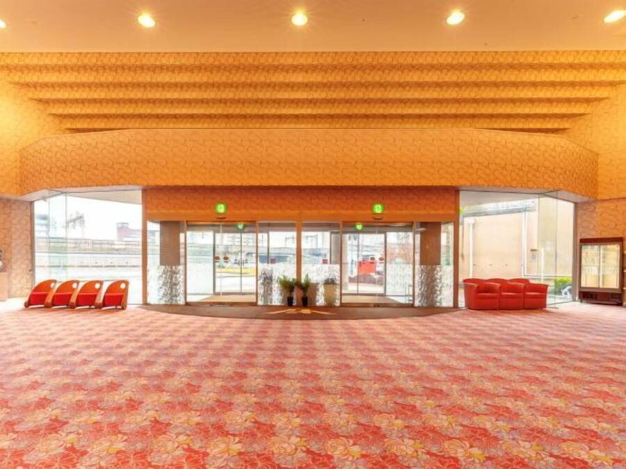 Un hall de hotel con alfombra estampada, un mostrador de recepción y una zona de estar con sillas rojas.