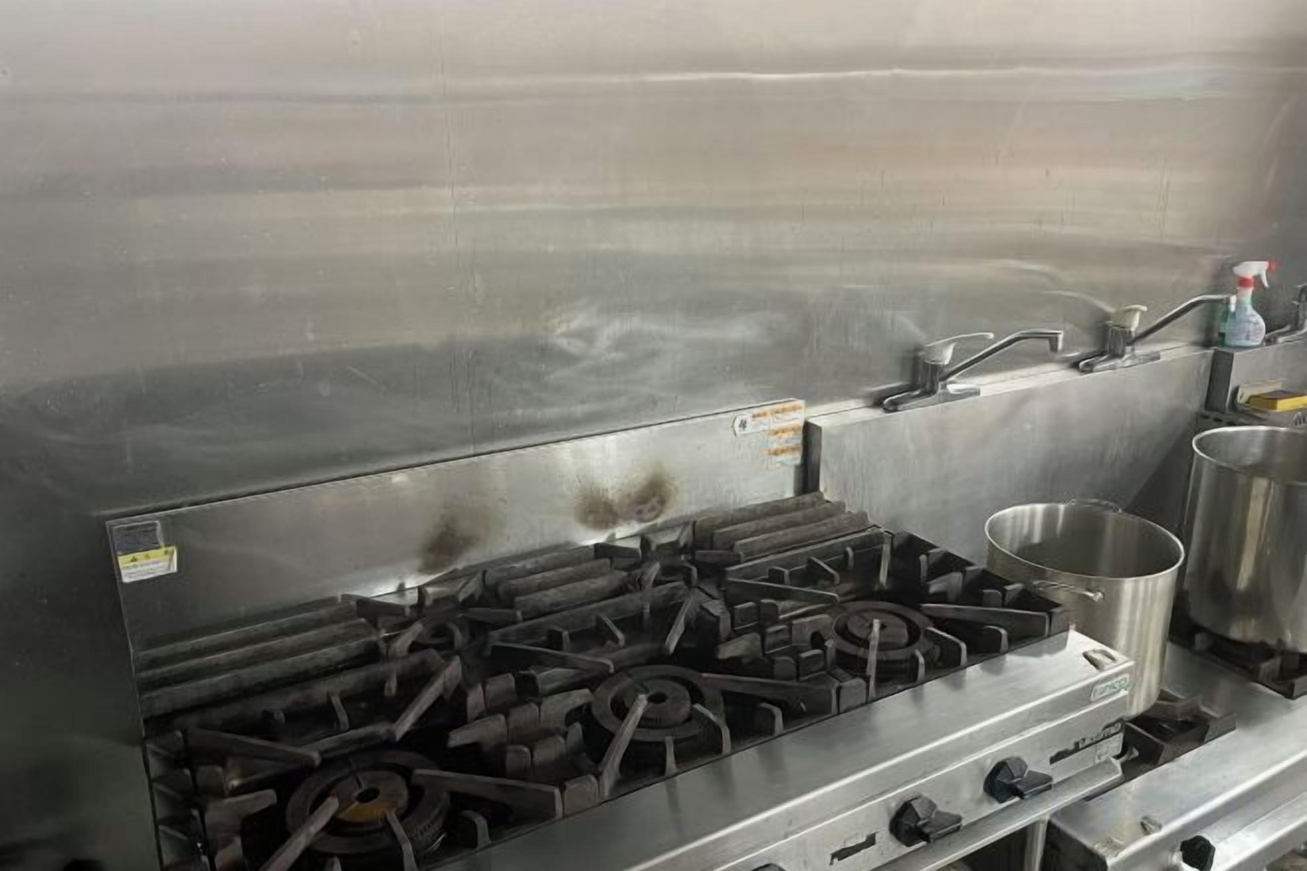 Una cocina de acero inoxidable con estufa a gas, un lavamanos y un recipiente metálico.