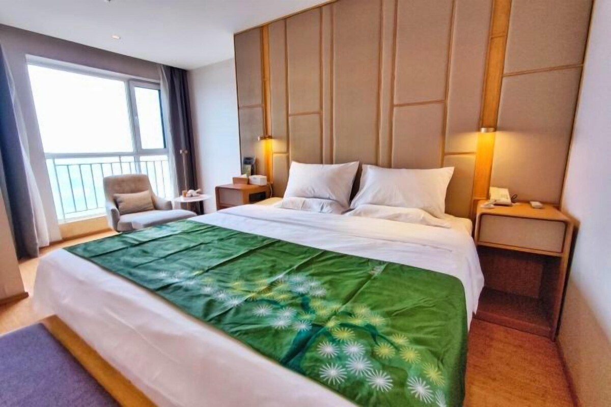 A hotel room with a large bed, a chair, a nightstand, and a window with a view.