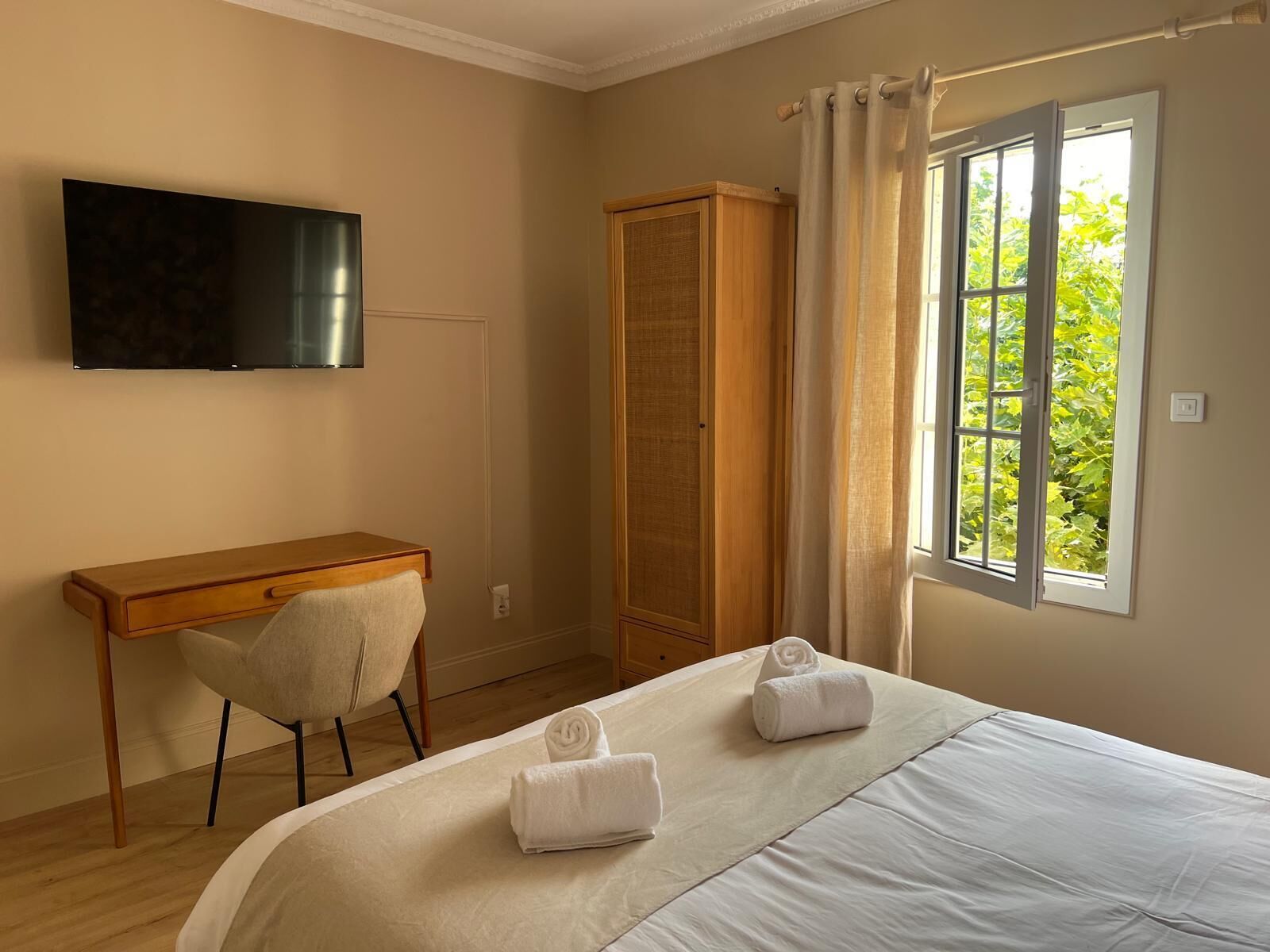 Een hotelkamer met een bed, een bureau, een stoel, een kledingkast, een televisie en een raam met uitzicht op groen.