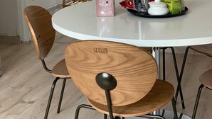 Un coin repas avec une table ronde blanche, des chaises en bois et une petite table sur laquelle sont disposés des plats et des boissons.