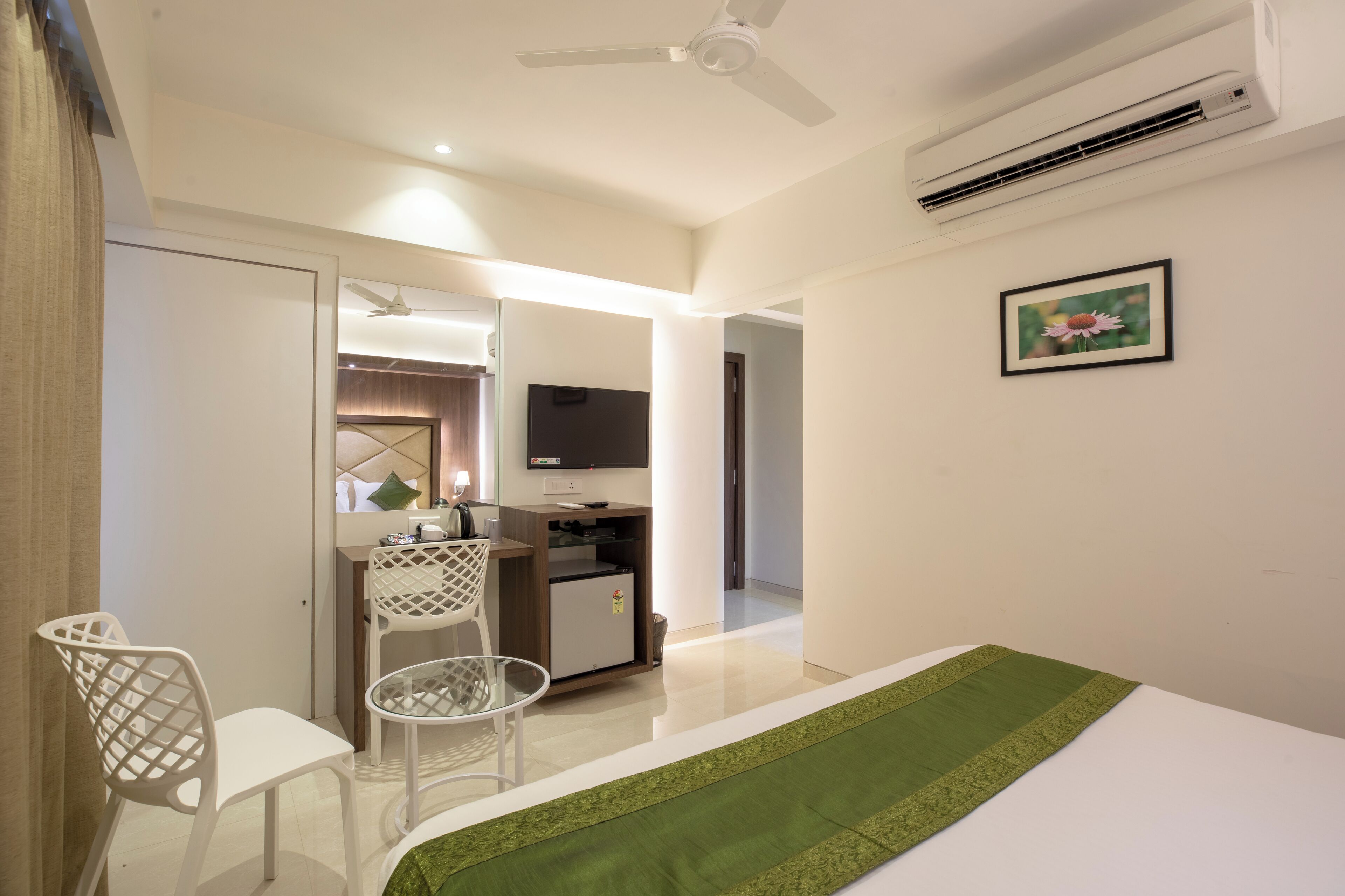 A hotel room with a bed, a desk, a chair, a television, and an air conditioning unit.