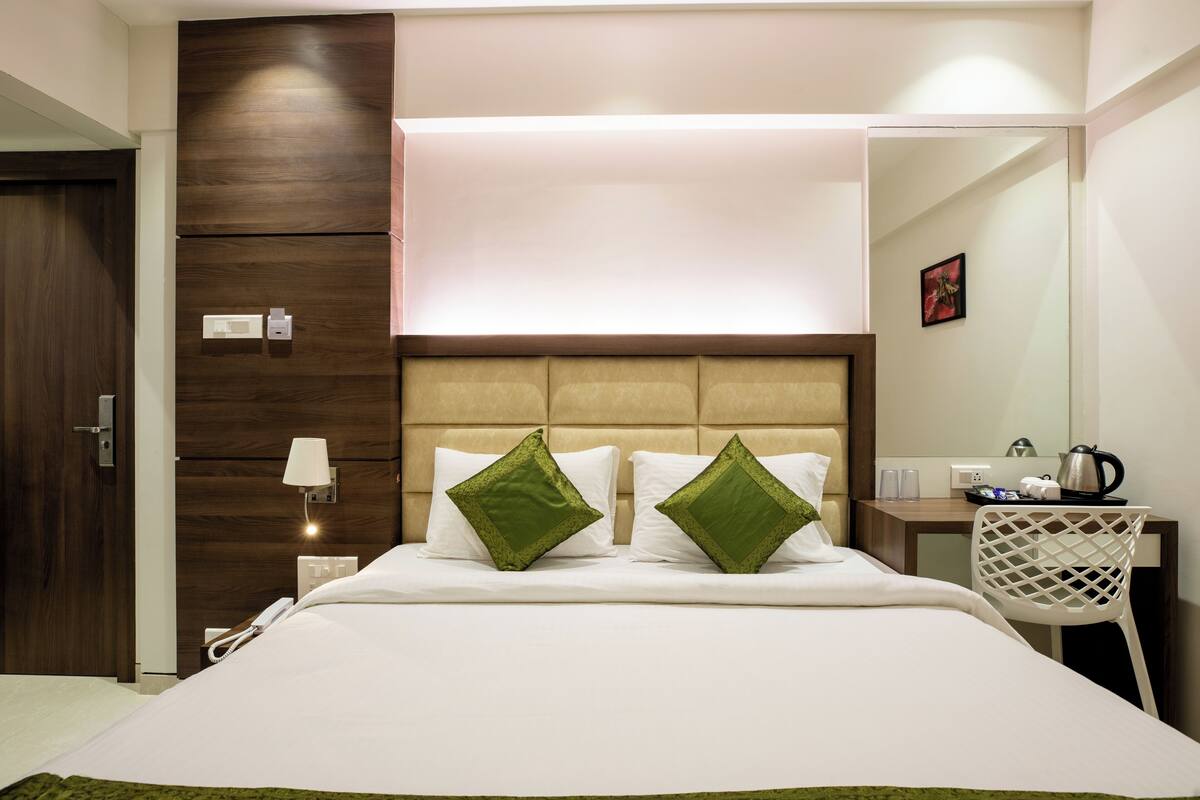 A hotel room with a bed, a desk with a chair, a mirror, and a door.