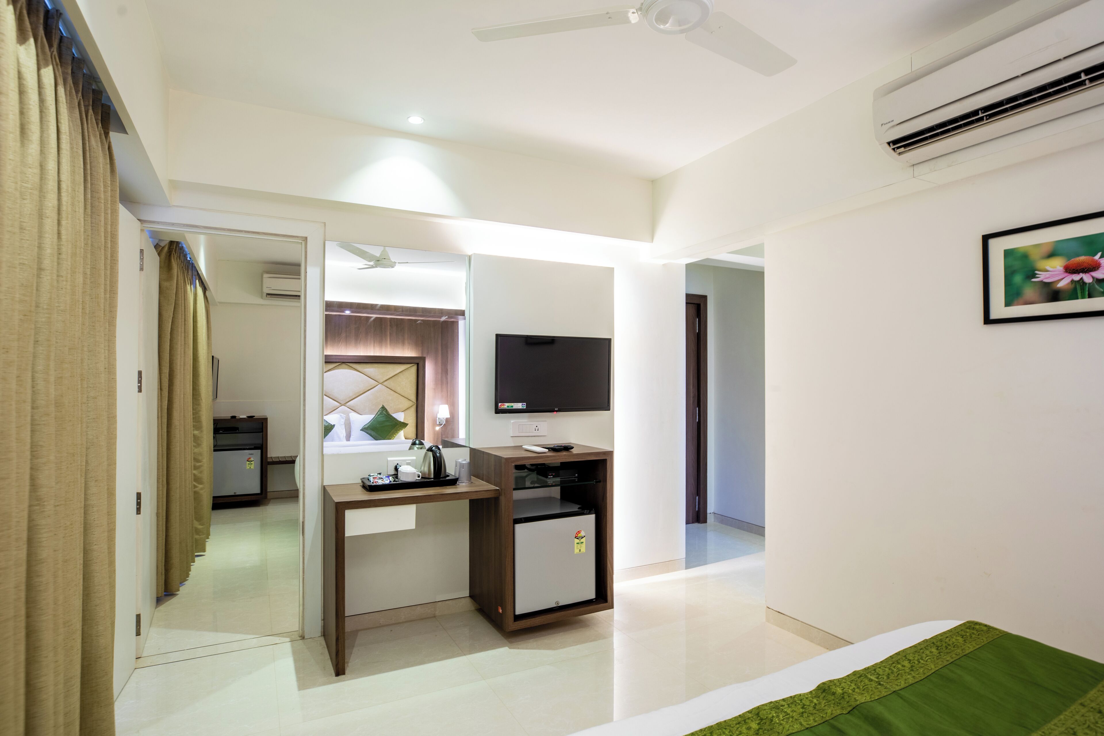 Una habitación de hotel con una cama, un escritorio con computadora, televisor y un refrigerador pequeño.