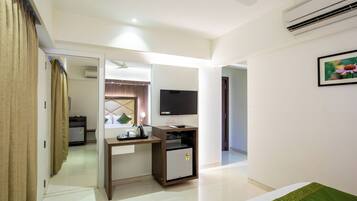 A hotel room with a bed, a desk with a computer, a television, and a small refrigerator.