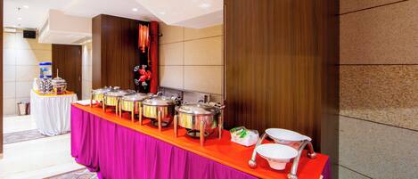 A buffet setup with multiple serving stations, a water dispenser, and a trash can.