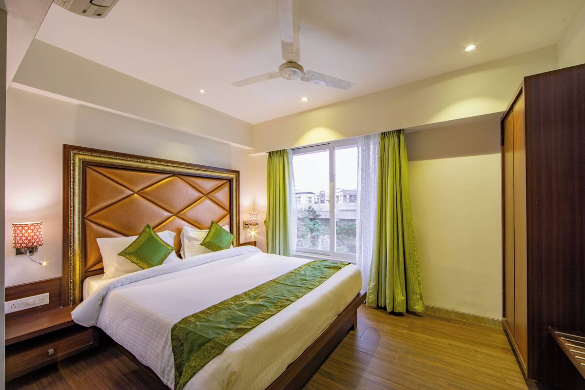 A hotel room with a large bed, a ceiling fan, a window with curtains, and a wardrobe.
