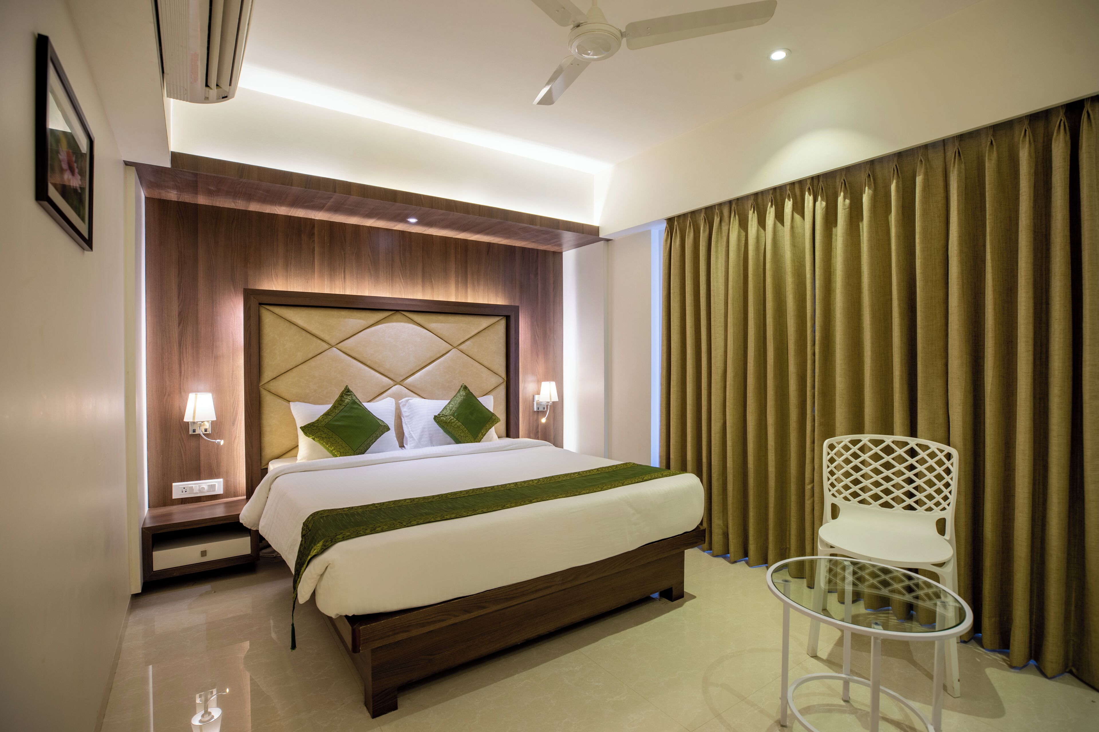 A hotel room with a bed, bedside tables, a chair, and a glass table.