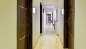 Un pasillo de hotel con suelo de mármol, puertas de madera e iluminación empotrada en el techo.