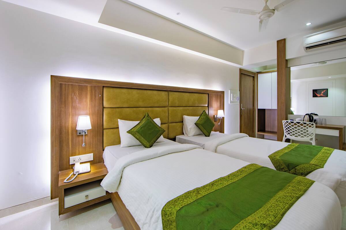 A hotel room with two beds, a wooden headboard, bedside lamps, a desk, and a mirror.
