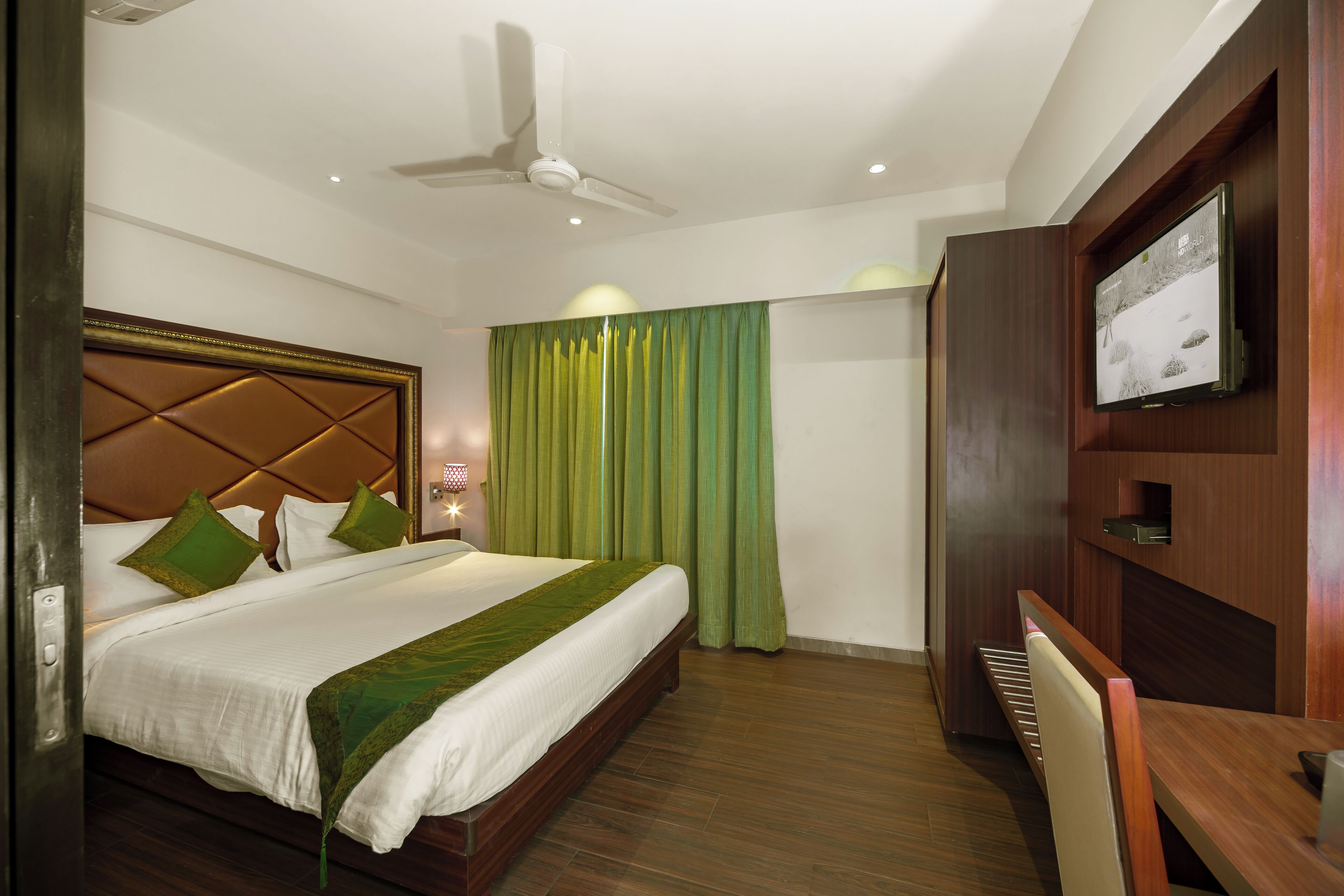 A hotel room with a bed, a desk, a television, and a ceiling fan.