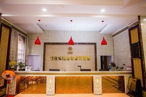 A reception area with a reception desk, two red pendant lights, and a wall with decorative elements. - Ayile Holiday Hotel (Yining City)