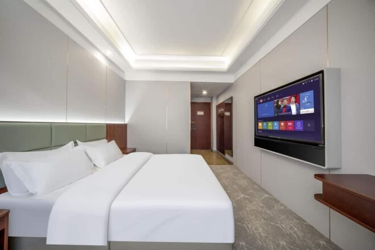 A modern hotel room with a large bed, a mounted TV, and a wooden nightstand.
