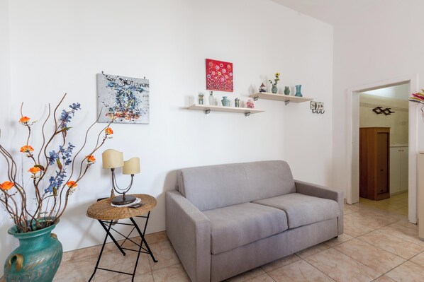 A living room with a grey sofa, a small round table with two lamps, a vase with flowers, and wall art. - 4061 Casa Wilma by Barbarhouse (Porto Cesareo)