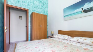 A bedroom with a bed, a wooden wardrobe, a nightstand, and a painting of a beach scene. - 4061 Casa Wilma by Barbarhouse (Porto Cesareo)