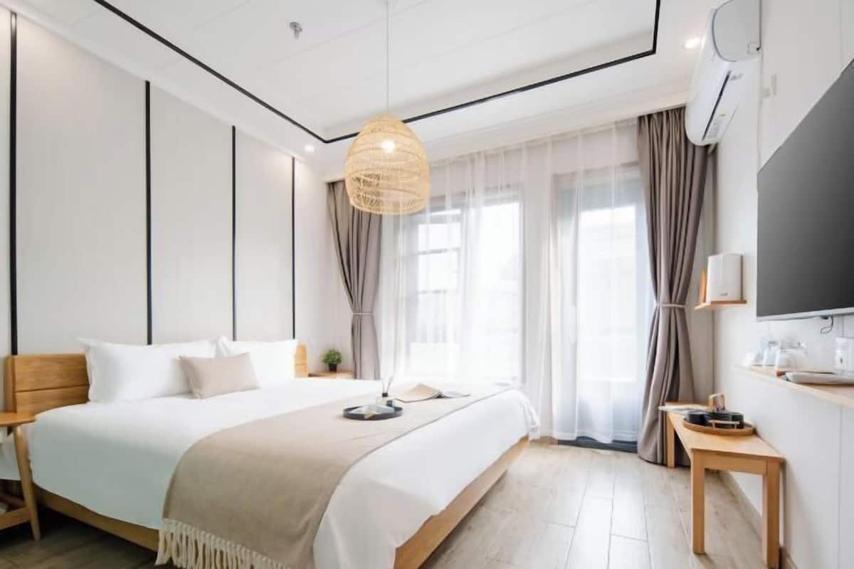 Una habitación de hotel moderna con una cama grande, una mesita de noche, un televisor y una ventana con cortinas.