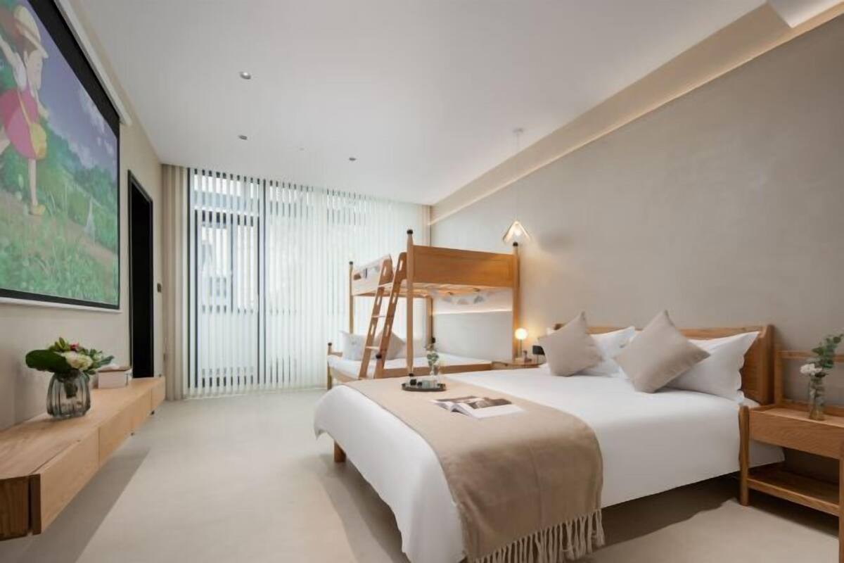 Un dormitorio moderno con una cama litera, una mesita de noche con lámpara, un ventanal con persianas y un cuadro en la pared.