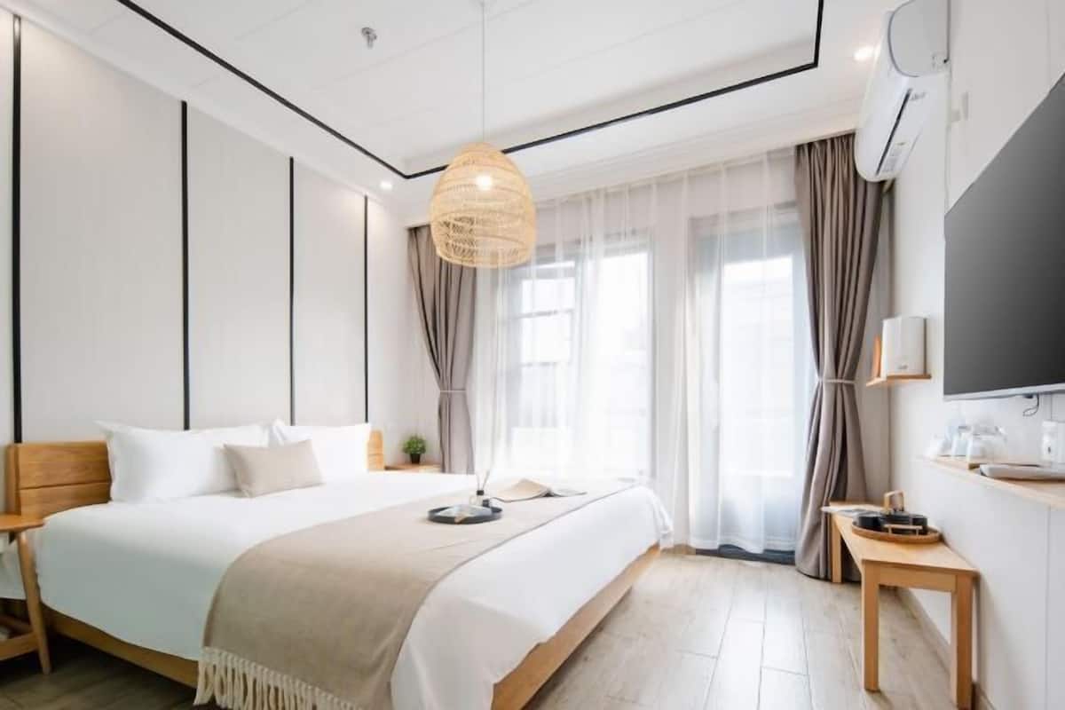 Una habitación de hotel moderna con una cama grande, mesitas de noche, un televisor y un ventanal con cortinas.