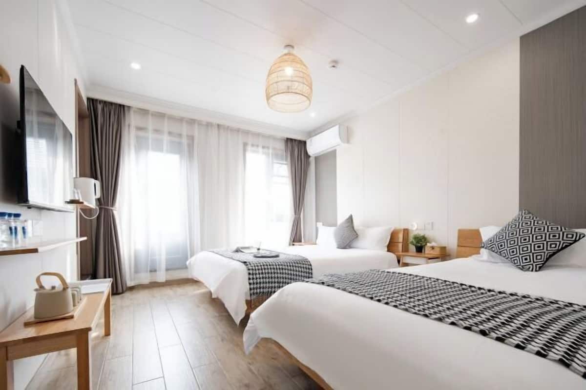 Habitación de hotel con dos camas, un televisor, una mesita de noche, una lámpara y una ventana con cortinas.