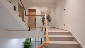 Een moderne trap met houten leuningen en een minimalistisch ontwerp, die uitkomt op een plateau met een deur en een kunstwerk aan de muur.