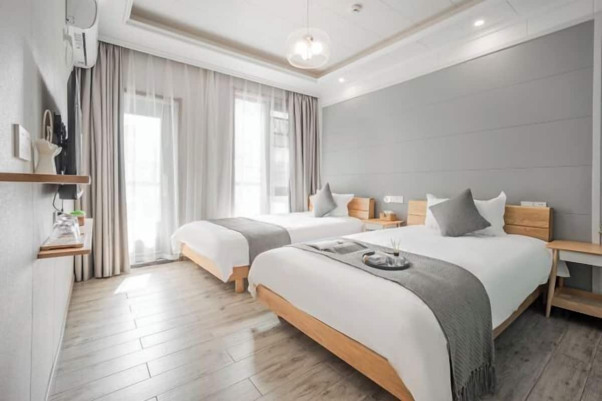 Una habitación de hotel moderna con dos camas, piso de madera, un ventanal con cortinas y un equipo de aire acondicionado instalado en la pared.