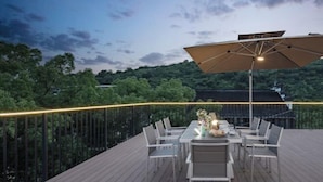 Een terras met een tafel, stoelen, een parasol en een hekwerk met verlichting.