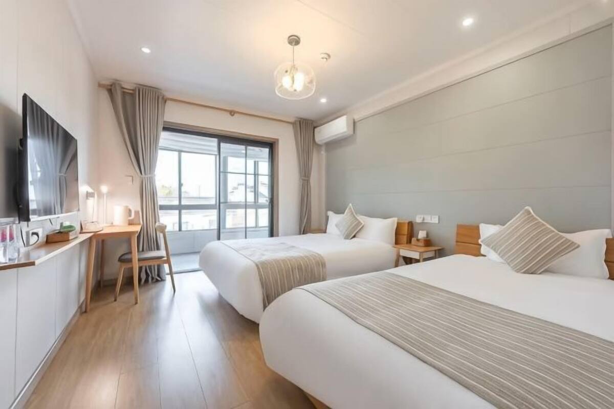 Habitación de hotel con dos camas, un escritorio, una silla, un televisor y una ventana con cortinas.