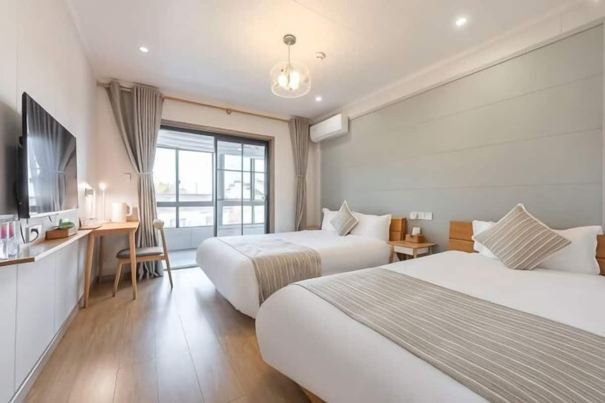 Ein Hotelzimmer mit zwei Betten, einem Schreibtisch, einem Stuhl, einem Fernseher und einem großen Fenster.